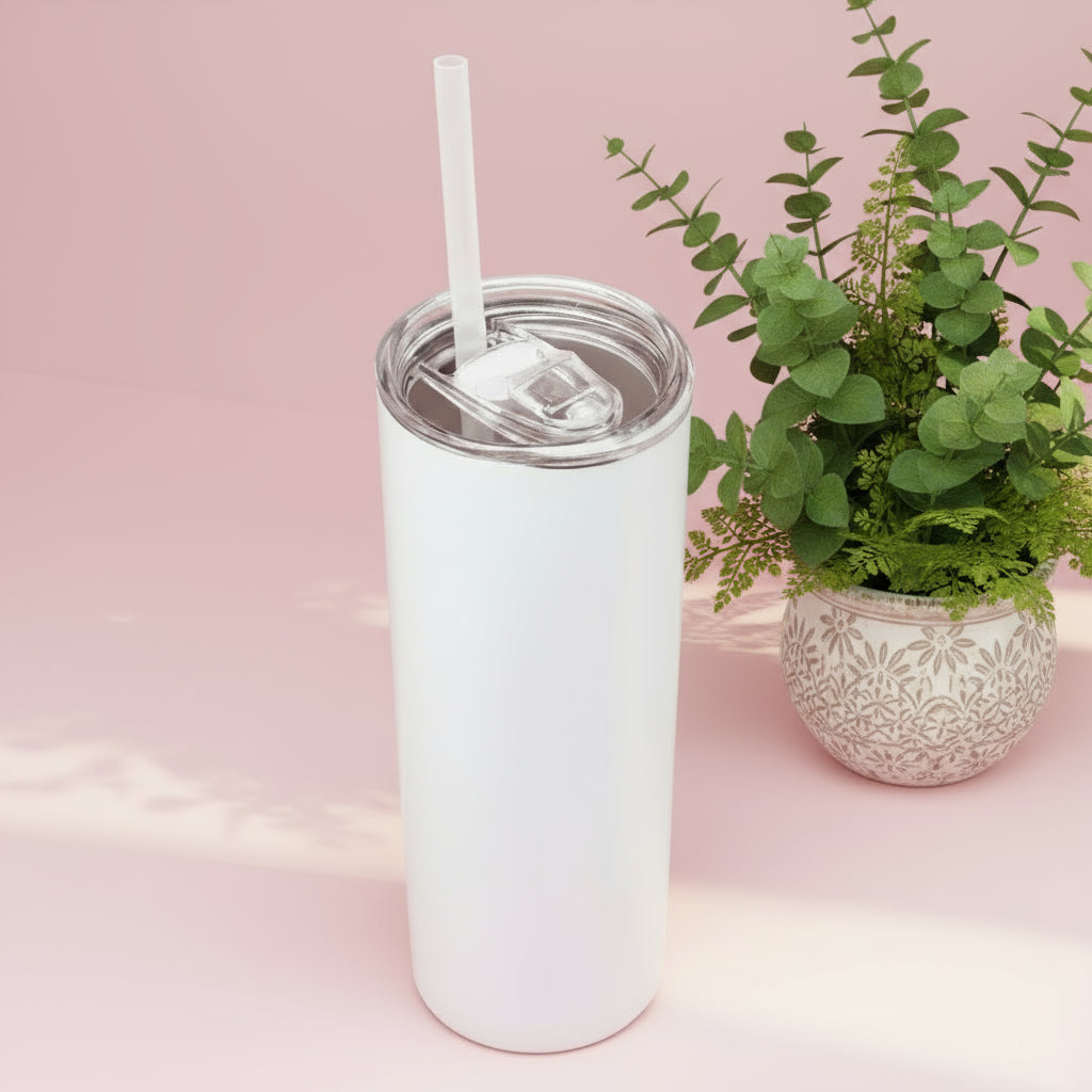 White tumbler with a straw next to a potted plant on a pink background