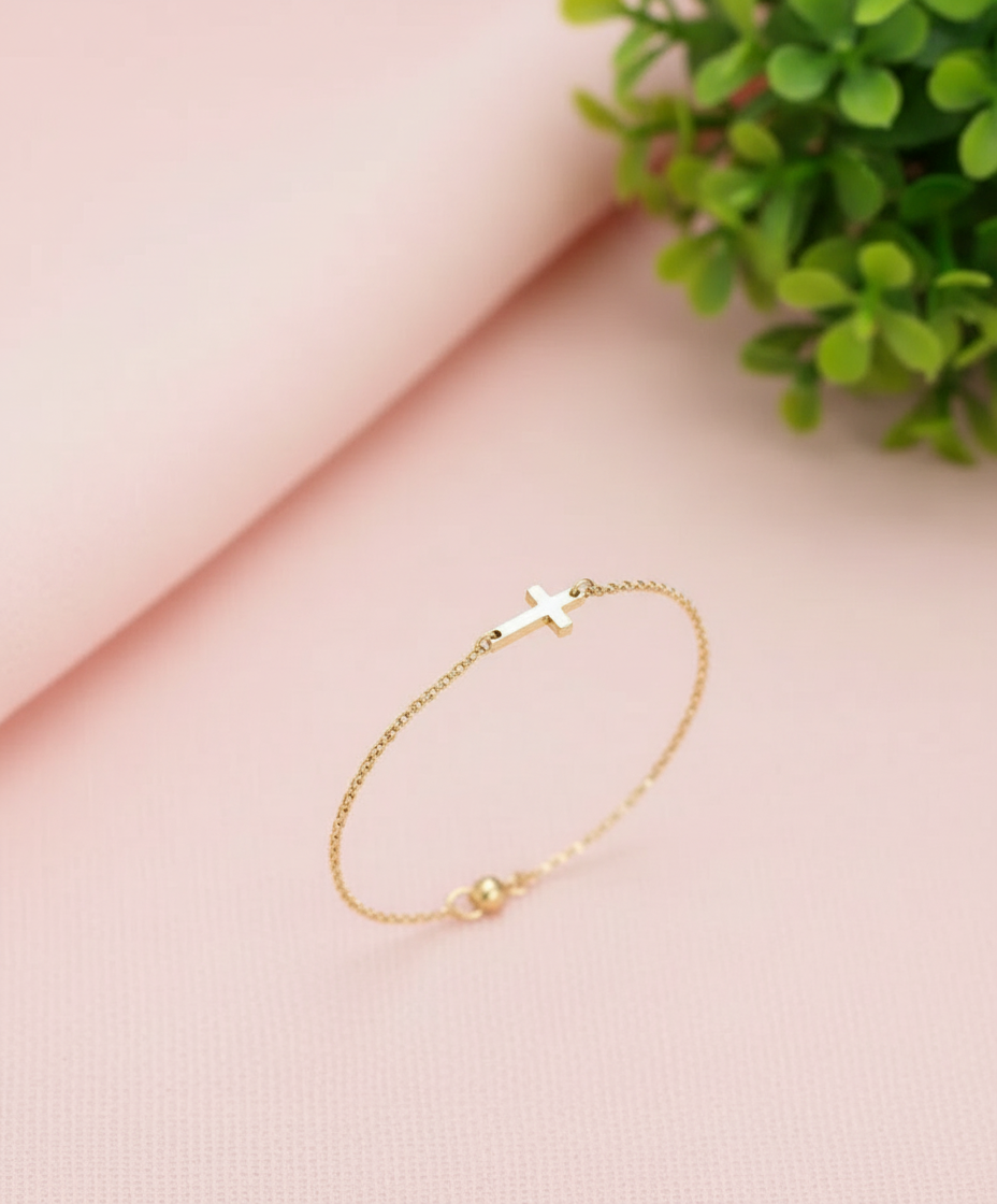 Gold bracelet with a cross charm on a wrist against a neutral background